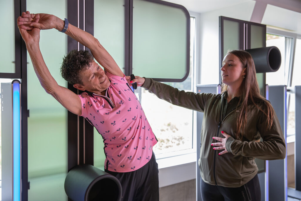 Vrouw krijgt hulp bij het uitoefenen van EGYM Smartflex mobiliteitsoefening