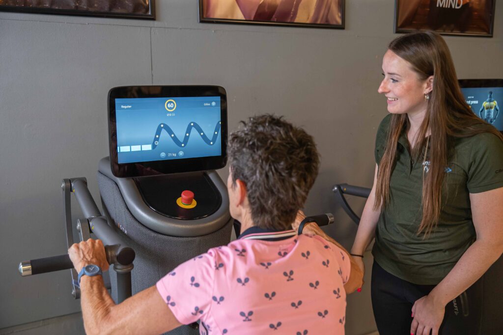Fysiotherapeut begeleidt oudere vrouw bij schouderoefening op EGYM-apparaat bij Intens Fit & Fysio