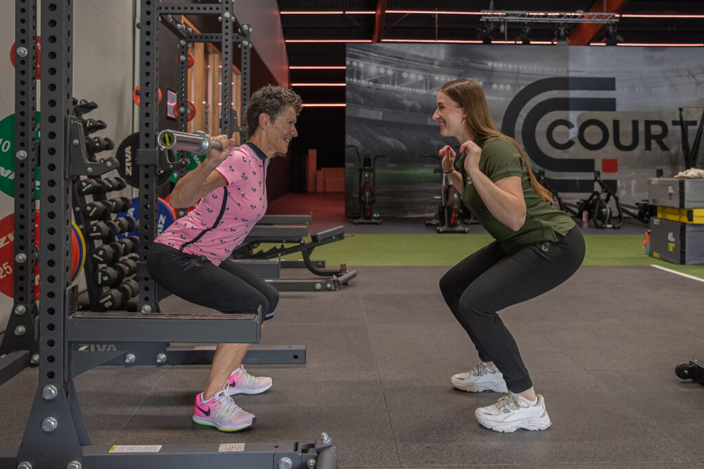 Squattraining door senior met hulp bij de vorm van de oefening door een trainer van Intens Fit & Fysio