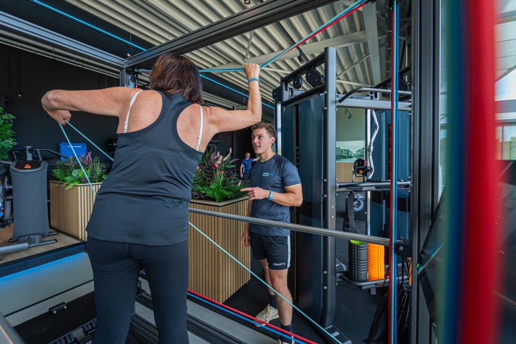 Vrouwelijke sporter zit op fitflex oefeningen uit te voeren onder begeleiding van een Fitcoach